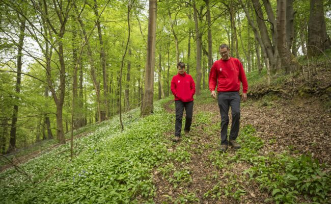 Two rangers in red uniform walking through a woodland