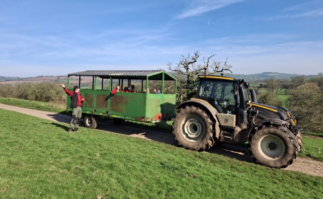 A large green tractor pulling a converted trailer with passengers.