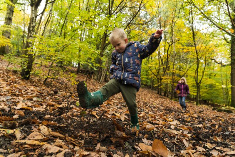 A child kicks up autumn leaves with his wellies