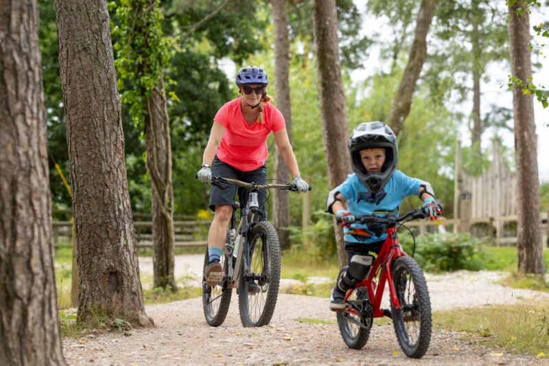 Adult and child riding mountain bikes on a surfaced forest trail