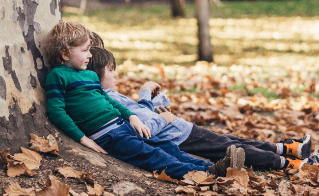 Devon in Autumn kids sitting near a tree in autumn leaves