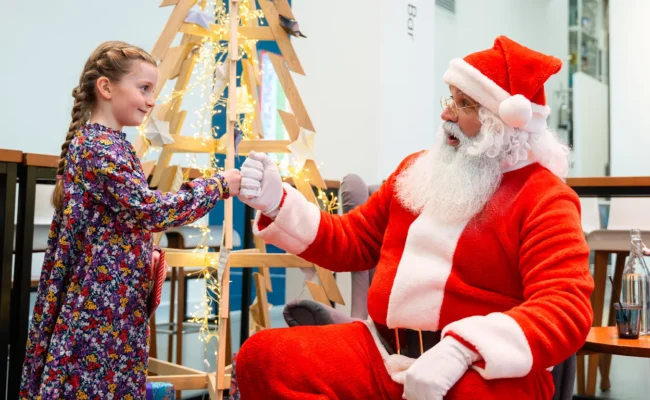 Photograph showing Father Christmas with a girl by a Christmas tree
