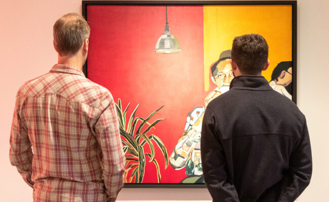 Two mean look at a large red, yellow and black painting on a gallery wall