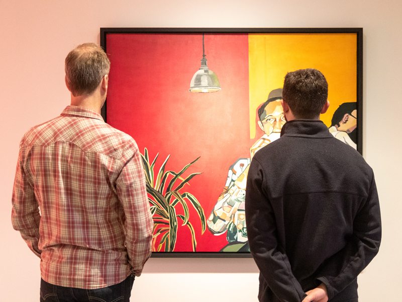 Two mean look at a large red, yellow and black painting on a gallery wall