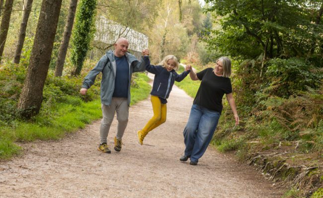 A couple walking on a wide forest track swing their daughter in the air between them