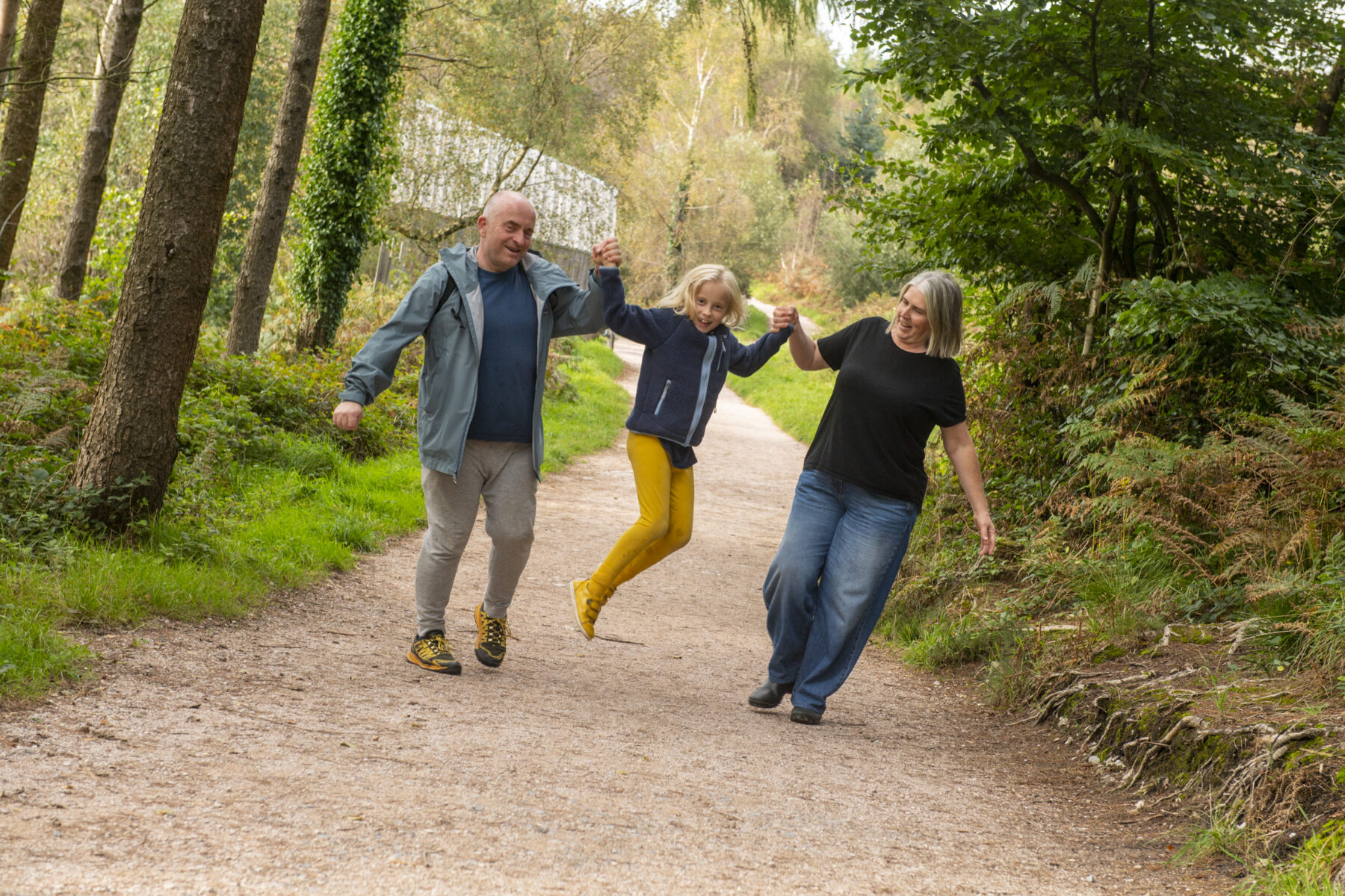 A couple walking on a wide forest track swing their daughter in the air between them