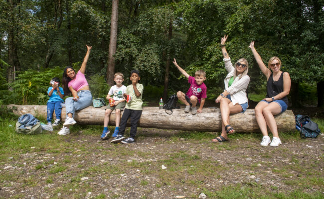 Family sitting on a large log wave to the camera