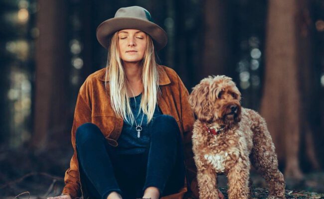 Photograph showing a woman and a dog sitting in a forest