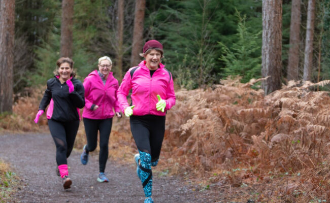 Three middle-aged women run through the forest