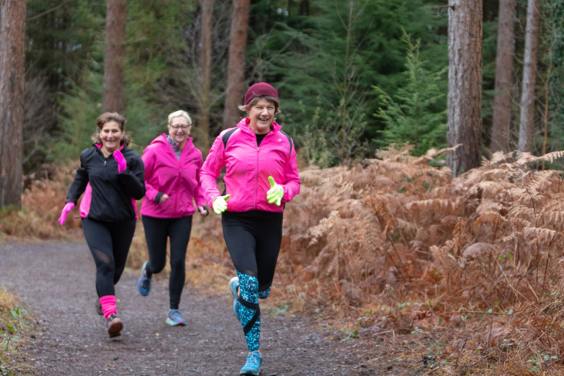 Three women running through the forest smiling