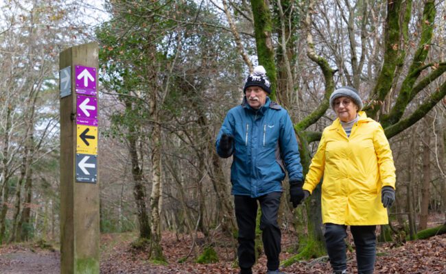 A couple walking on a forest trail in coats and bobble hats