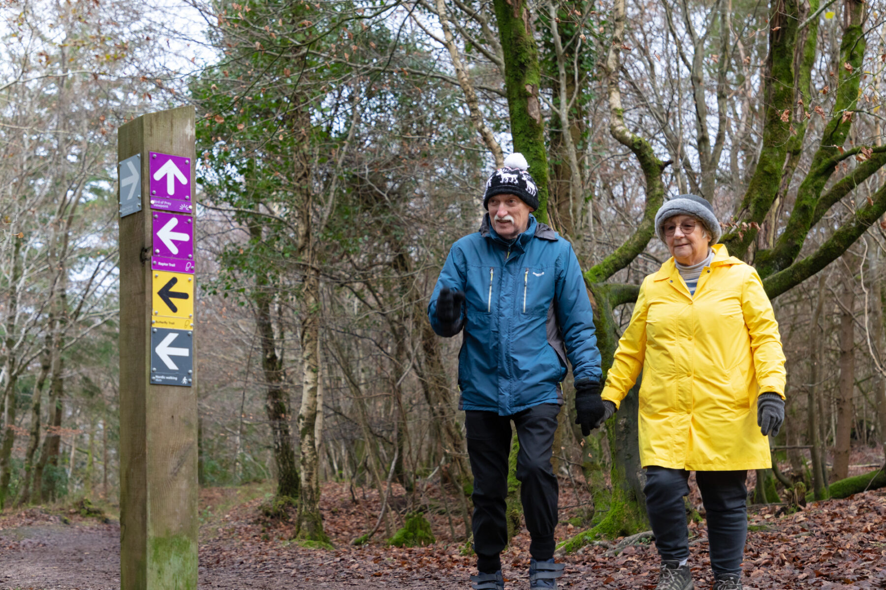 A couple walking on a forest trail in coats and bobble hats