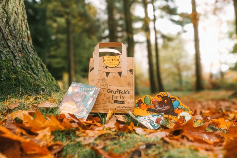 A brown paper bag sits among autumn leaves surrounded by activity materials