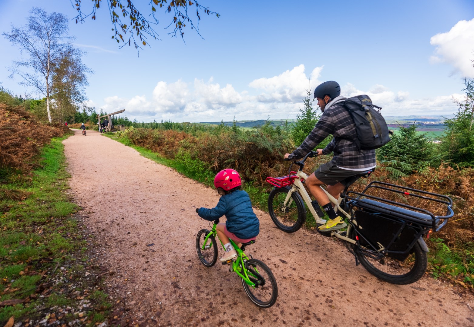 An adult and a child cycle along a flat wide forest track