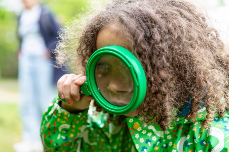 A young girl holding a magnifying glass to close to her eye.