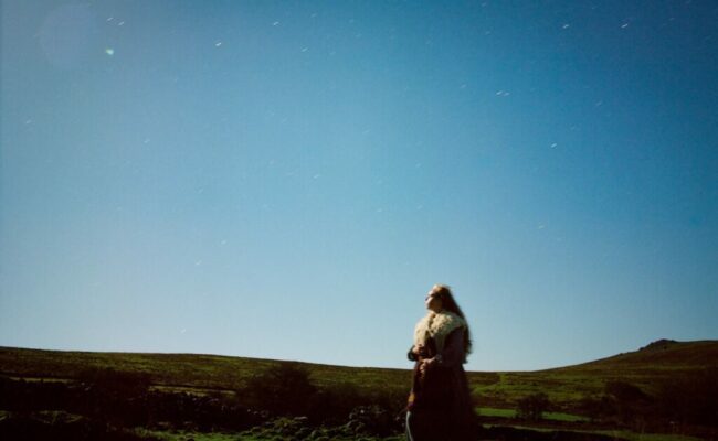a woman wanders on a hilltop landscape and watches the sunset