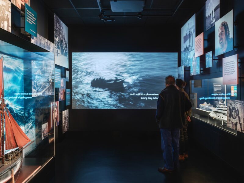 Two people watch a film projection in a dark gallery