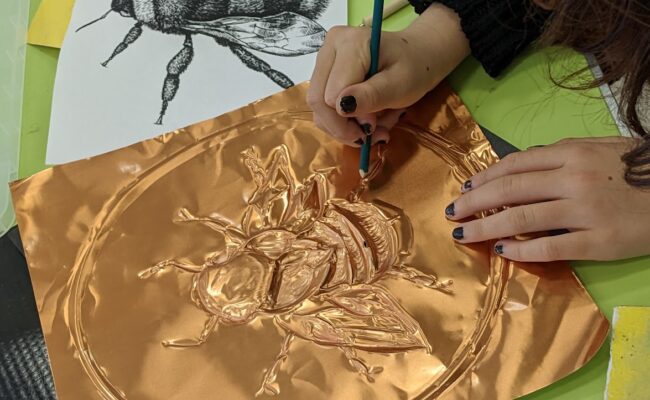 Child embossing a picture of a bee onto a bronze metal material
