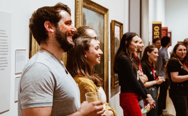 smiling members of audience standing along a gallery wall.