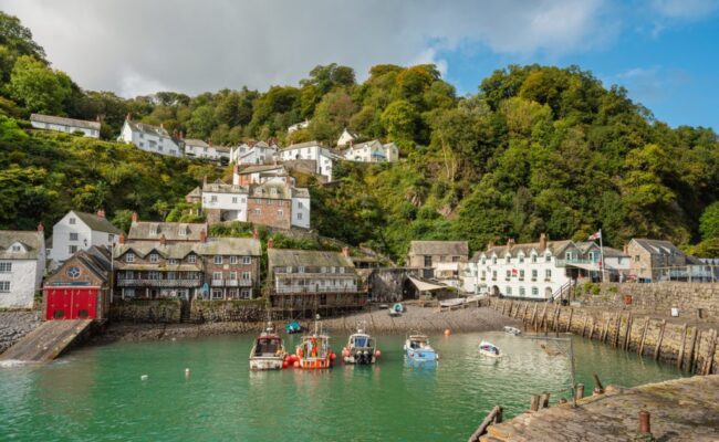 Stone buildings nestled into a cliff with a harbour at the bottom with blue sea and boats floating