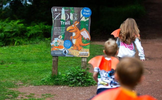 Children wearing orange cardboard dragon wings running towards a sign that says Zog Trail