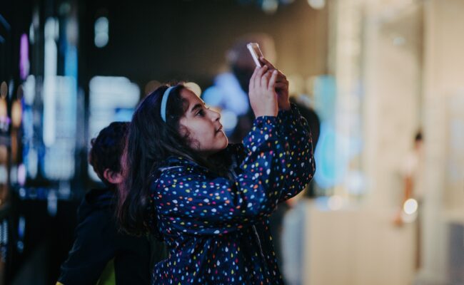 A girl in a blue coat takes a photo on her mobile device