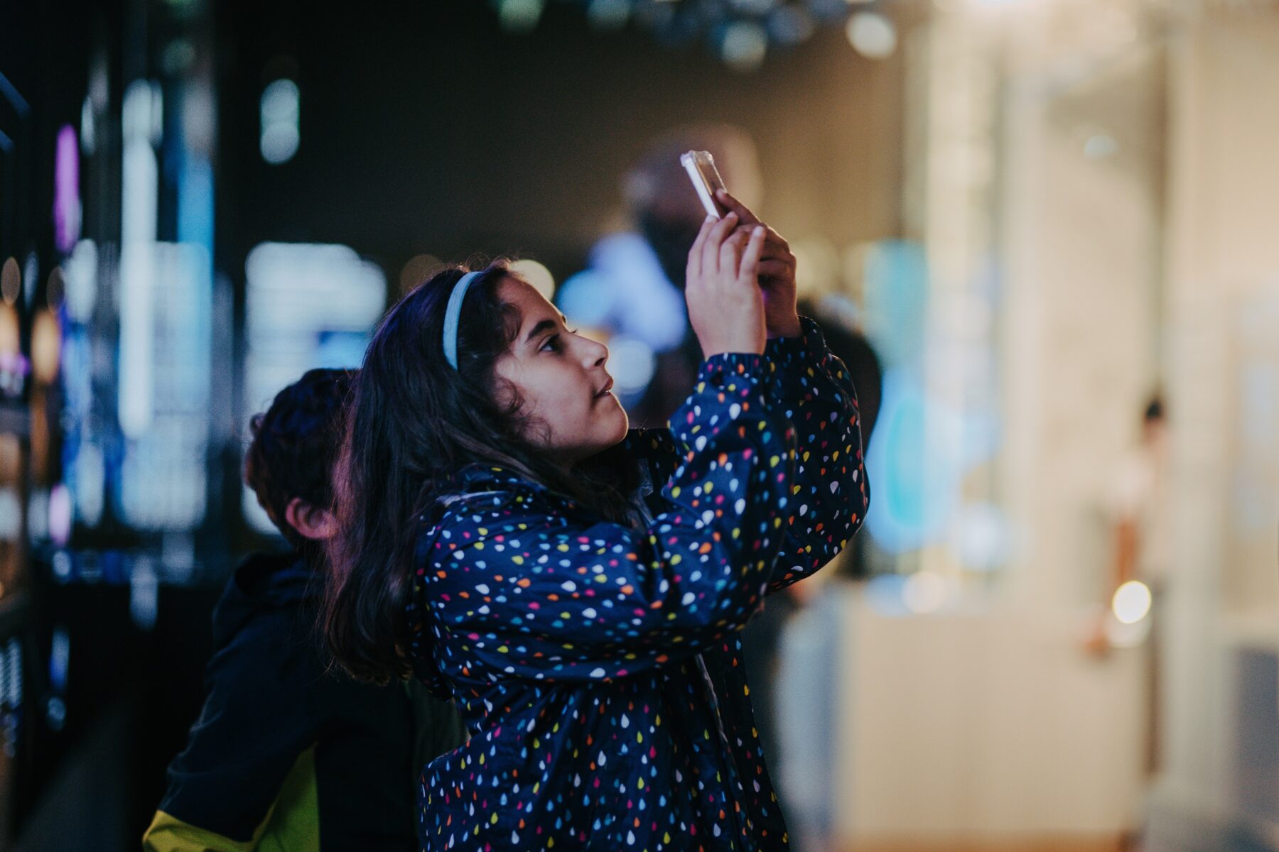 A girl in a blue coat takes a photo on her mobile device