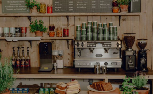 Coffee serving counter with coffee machine, cups, syrups, and other accessories.