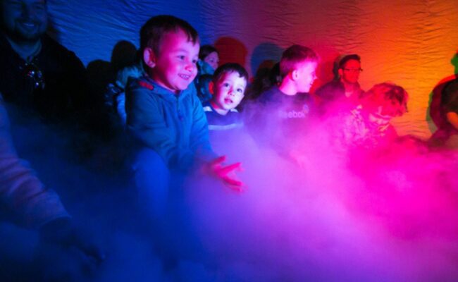 young children surrounded by colourful lights and fog, looking excited and smiling
